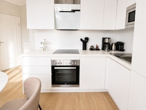 A modern kitchen with white cabinetry, a built-in oven, a microwave, and a coffee maker. - Welcome to TECHTS - TECHTs Strandhaus (Timmendorfer Strand)
