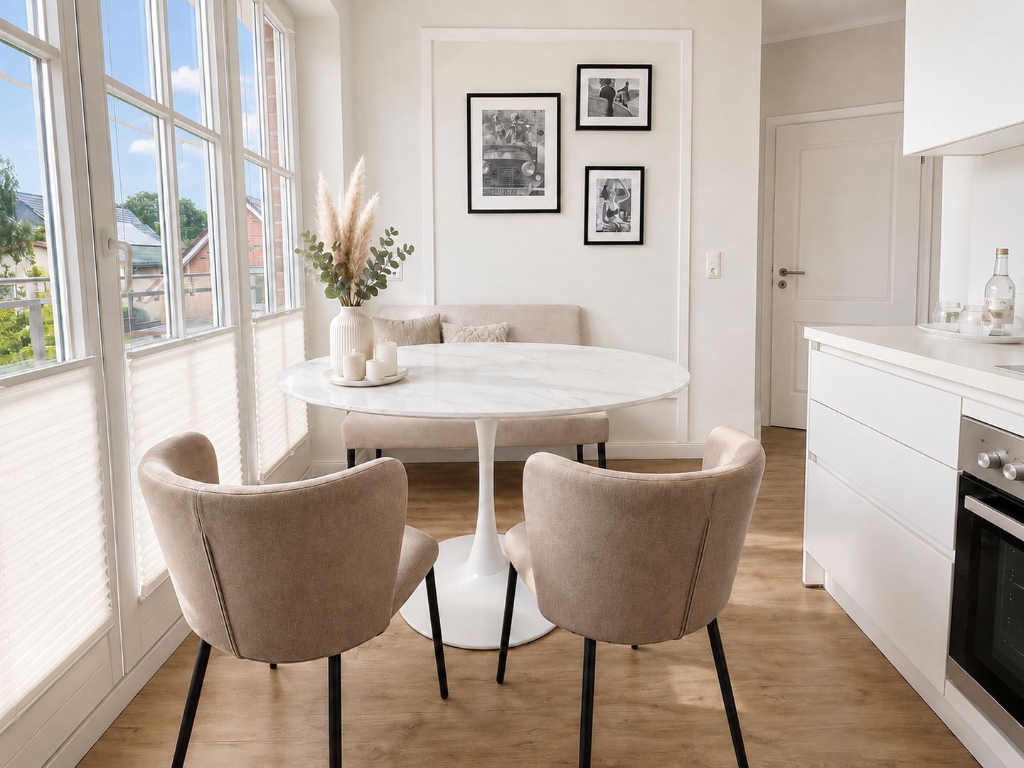 A modern kitchen with a round dining table, two chairs, a white cabinet, and a window with blinds.