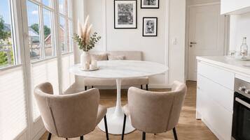 A modern kitchen with a round dining table, two chairs, a white cabinet, and a window with blinds.