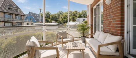A balcony with a sofa, two chairs, a small table, and a potted plant.
