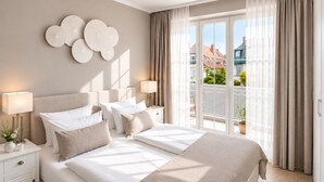 A hotel room with a large bed, two bedside tables, a lamp, and a view of the city through a balcony. - Welcome to TECHTS - TECHTs Strandhaus (Timmendorfer Strand)