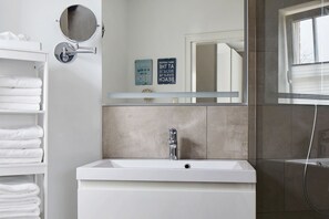 Un baño con un lavamanos blanco, un espejo redondo, un perchero y una ducha.