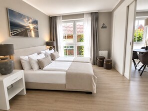 Une chambre moderne avec un grand lit, des tables de chevet, un bureau et une vue sur l’extérieur.