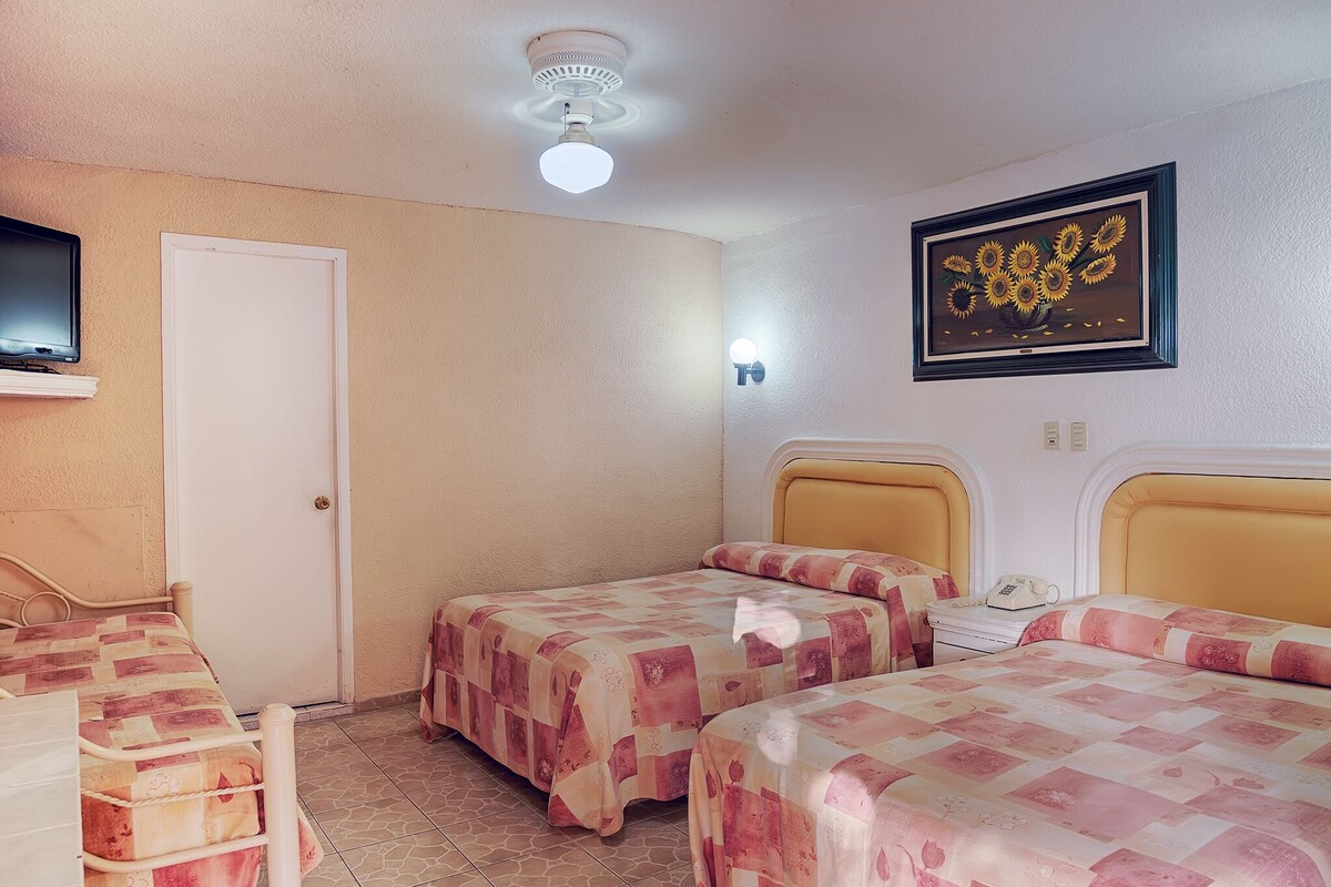 Ein Zimmer mit zwei Betten, einem Sessel, einem Fernseher und einem gerahmten Bild an der Wand.