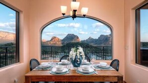 A dining area with a table set for four, a chandelier, and a view of mountains through a large arched window. - Zen Retreat, Amazing Views, Minutes to Attractions (Sedona)