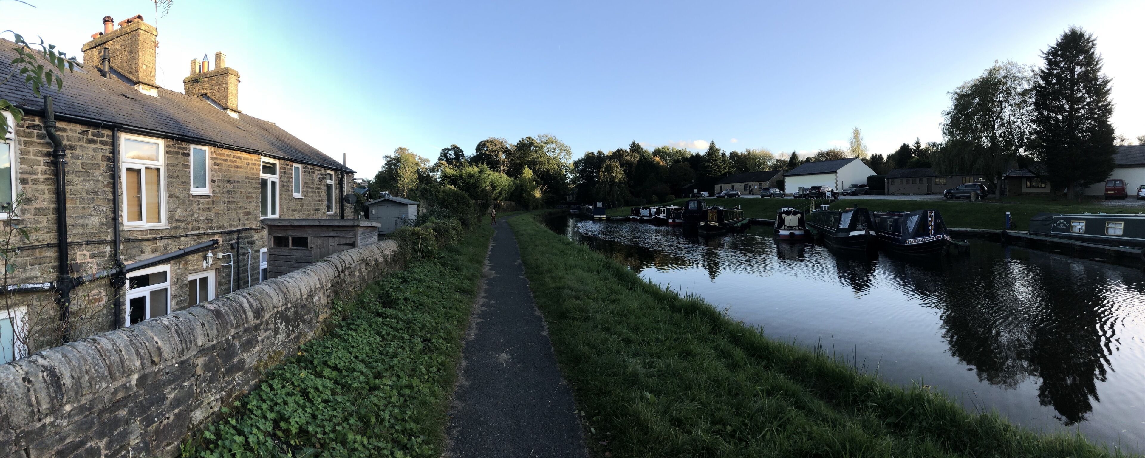 A narrow canal with boats docked on the right, flanked by stone buildings and greenery.