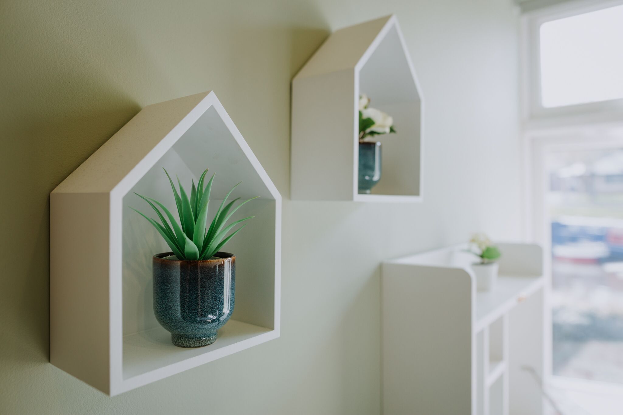A wall with two geometric shelves, each containing a plant.