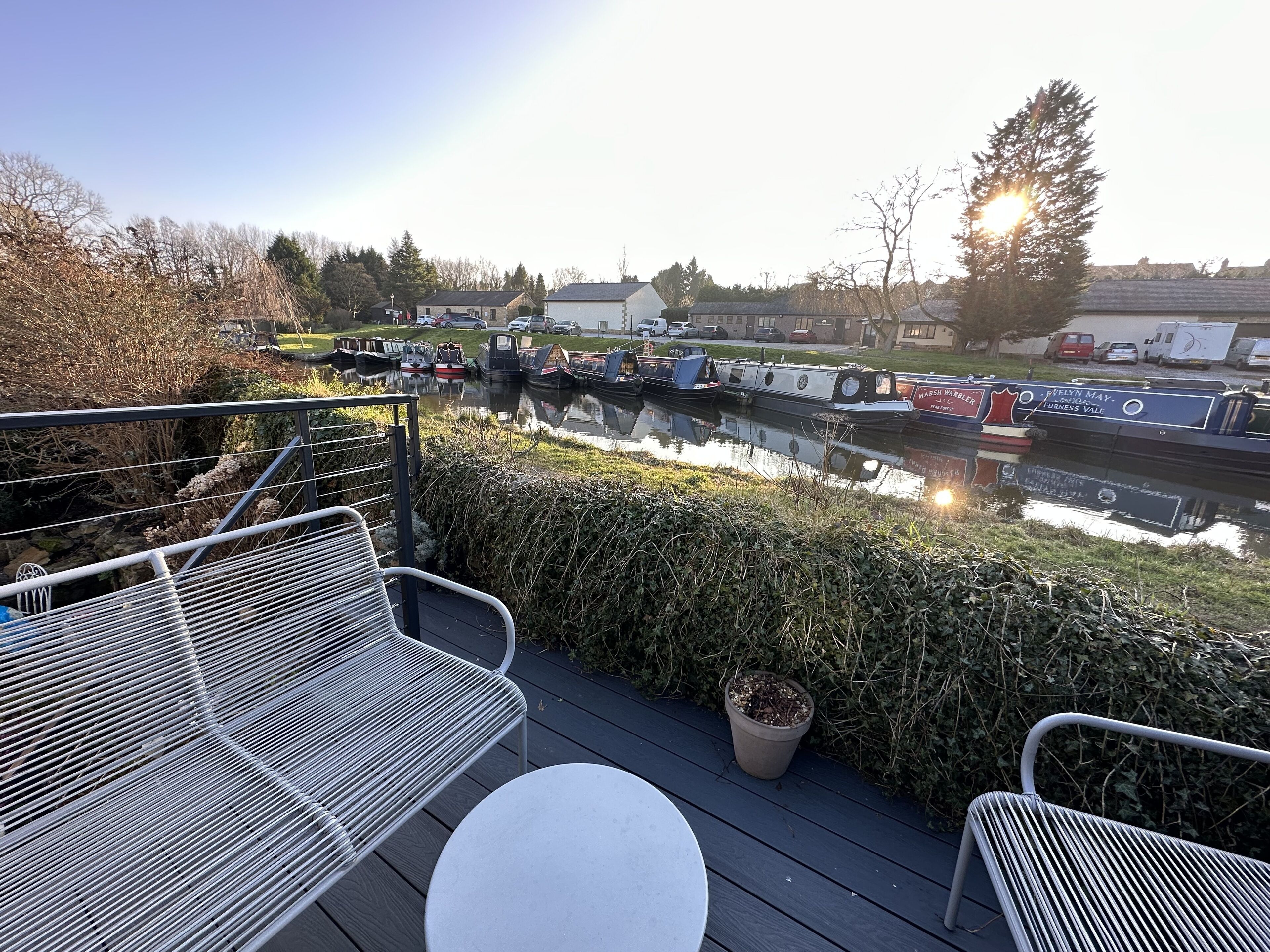 Una terraza con sillas metálicas y una mesa con vista a un canal con barcos.