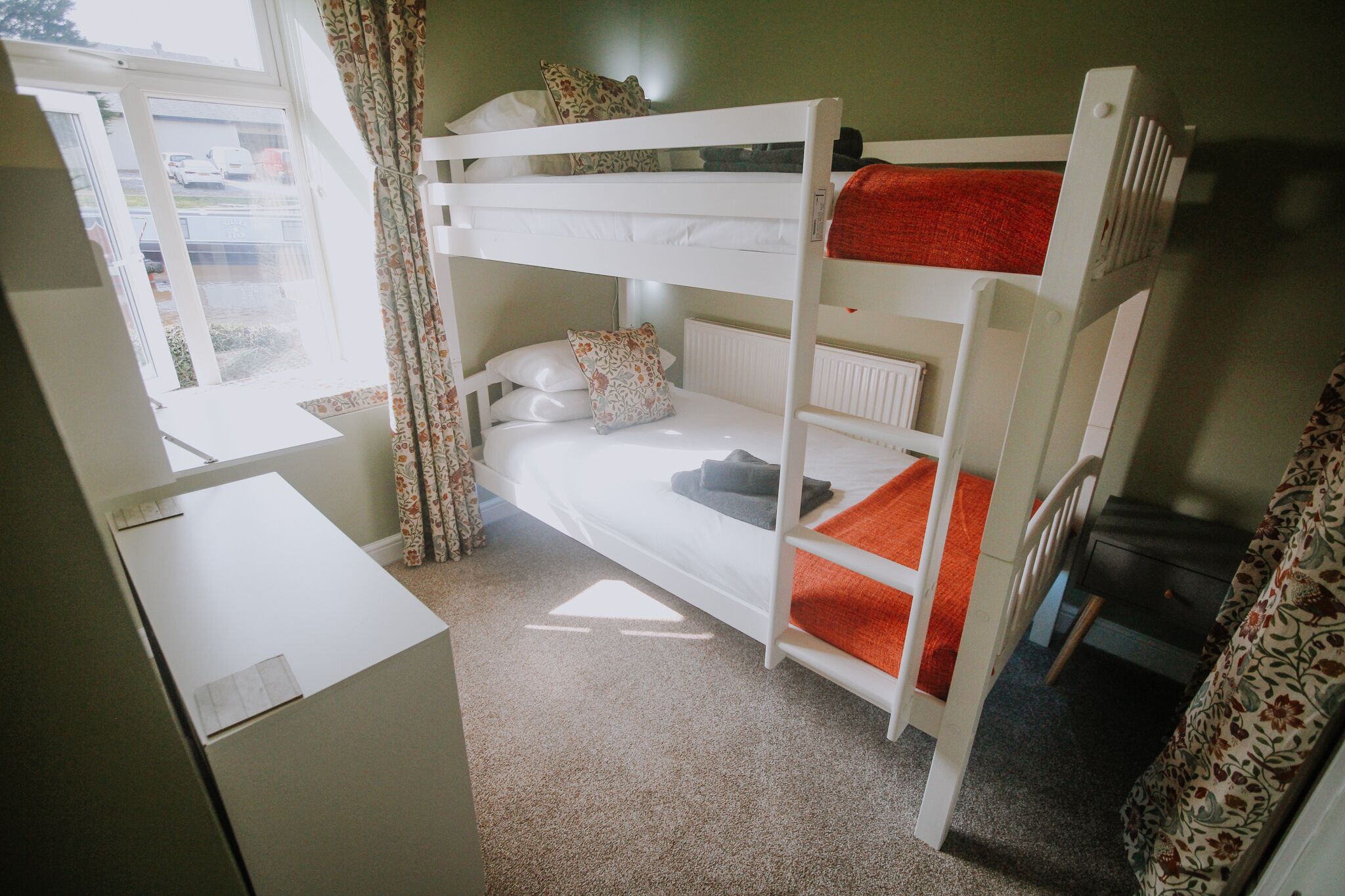 A bunk bed room with a desk and a window.
