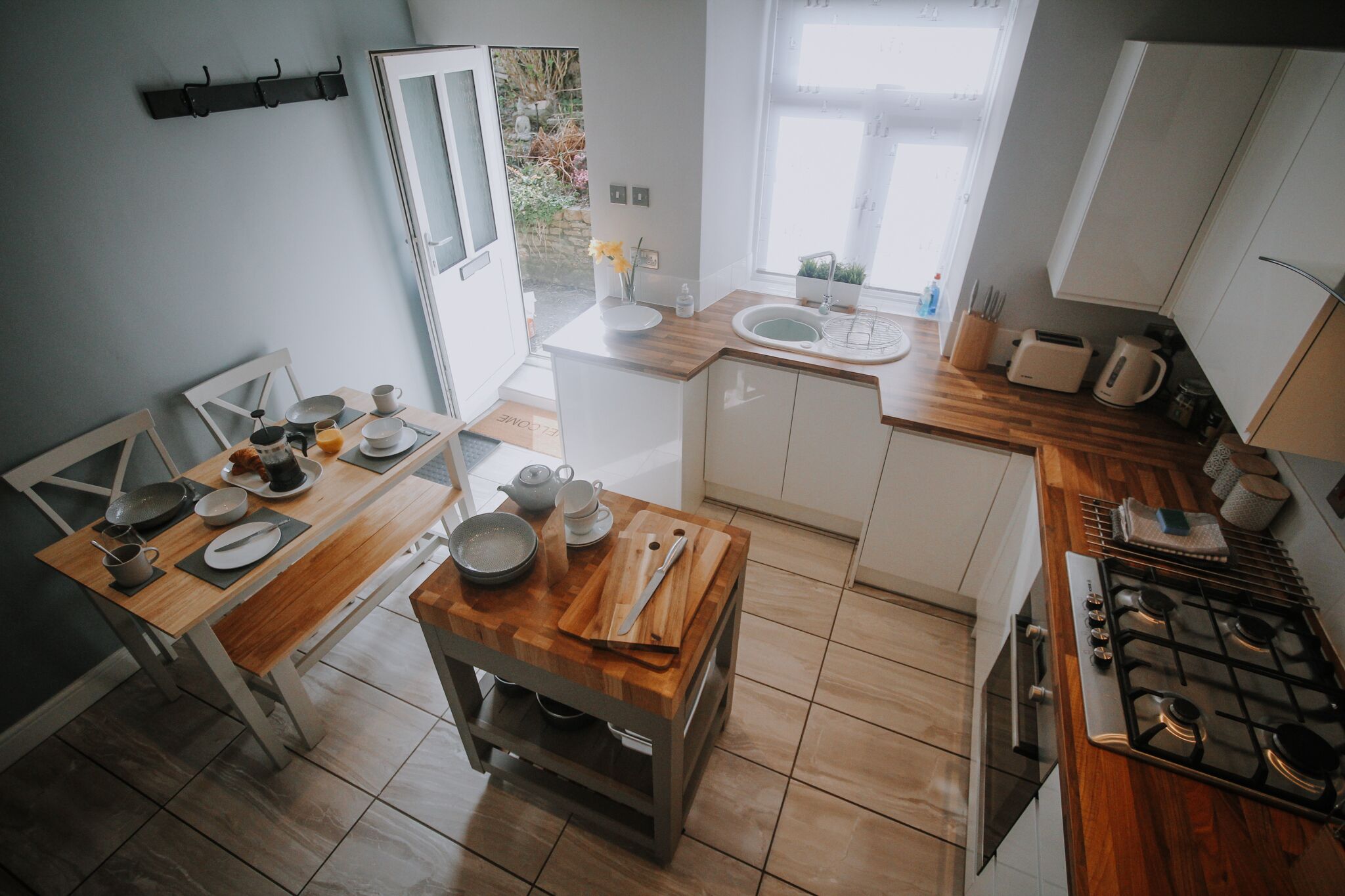 Una cucina compatta con un tavolo da pranzo in legno, mobili bianchi e un piano cottura a gas.