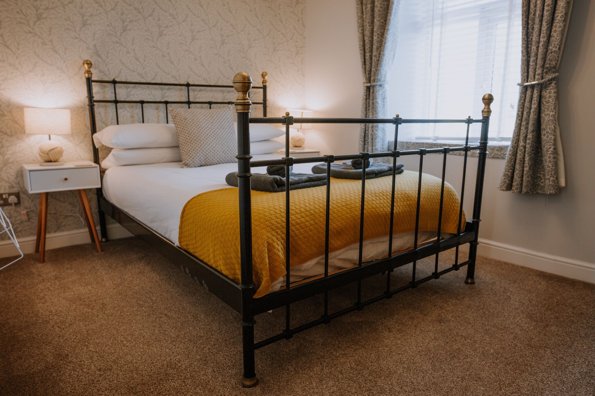 A neatly made bed with a black metal frame, white bedding, and a mustard-colored throw.