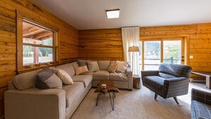 Interior acolhedor de uma cabana de madeira com um sofá seccional, uma poltrona xadrez e uma pequena mesa de centro.