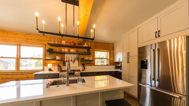 Uma cozinha moderna com uma ilha grande, eletrodomésticos de aço inoxidável, detalhes em madeira e uma luminária pendente.