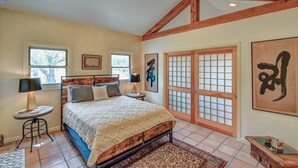 A bedroom with a bed, two bedside tables, a window, a door with a grid pattern, and artwork on the walls. - M'walimu 4 BR w/ Pool, Farm Stay- Flower Farm, Goats, Pigs, Disc Golf! (Glen Rose)