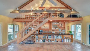A spacious library with a wooden staircase, bookshelves, and a ceiling fan. - M'walimu 4 BR w/ Pool, Farm Stay- Flower Farm, Goats, Pigs, Disc Golf! (Glen Rose)