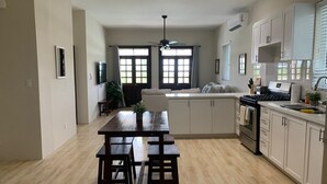 A modern kitchen with a central island, wooden dining table, and white cabinetry. - The Cedar Canalfront Penthouse (Nassau)