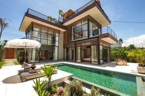 Una casa moderna de dos pisos con piscina, ventanas amplias y mobiliario exterior.