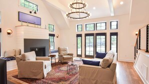A spacious living room with a fireplace, multiple seating areas, and large windows. - Luxurious, Modern Walk to Water! (Orleans)