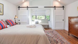 A bedroom with a bed, a bench, a dresser, and a window with a view of greenery. - Luxurious, Modern Walk to Water! (Orleans)