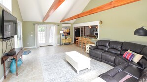 Un salon spacieux avec un canapé en cuir noir, une table basse blanche et un téléviseur posé sur un meuble en bois.