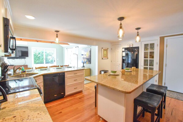 A modern kitchen with a dishwasher, double sink, and a large island with stools.