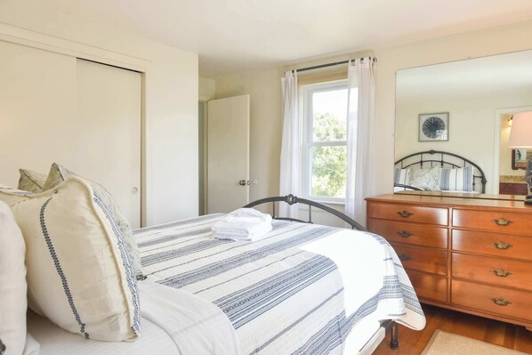 A bedroom with a bed, a dresser, a window with curtains, and a door. - Steps to water, easy access to town center! (Wellfleet)