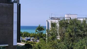 A building with a view of the ocean, surrounded by greenery and parked cars.