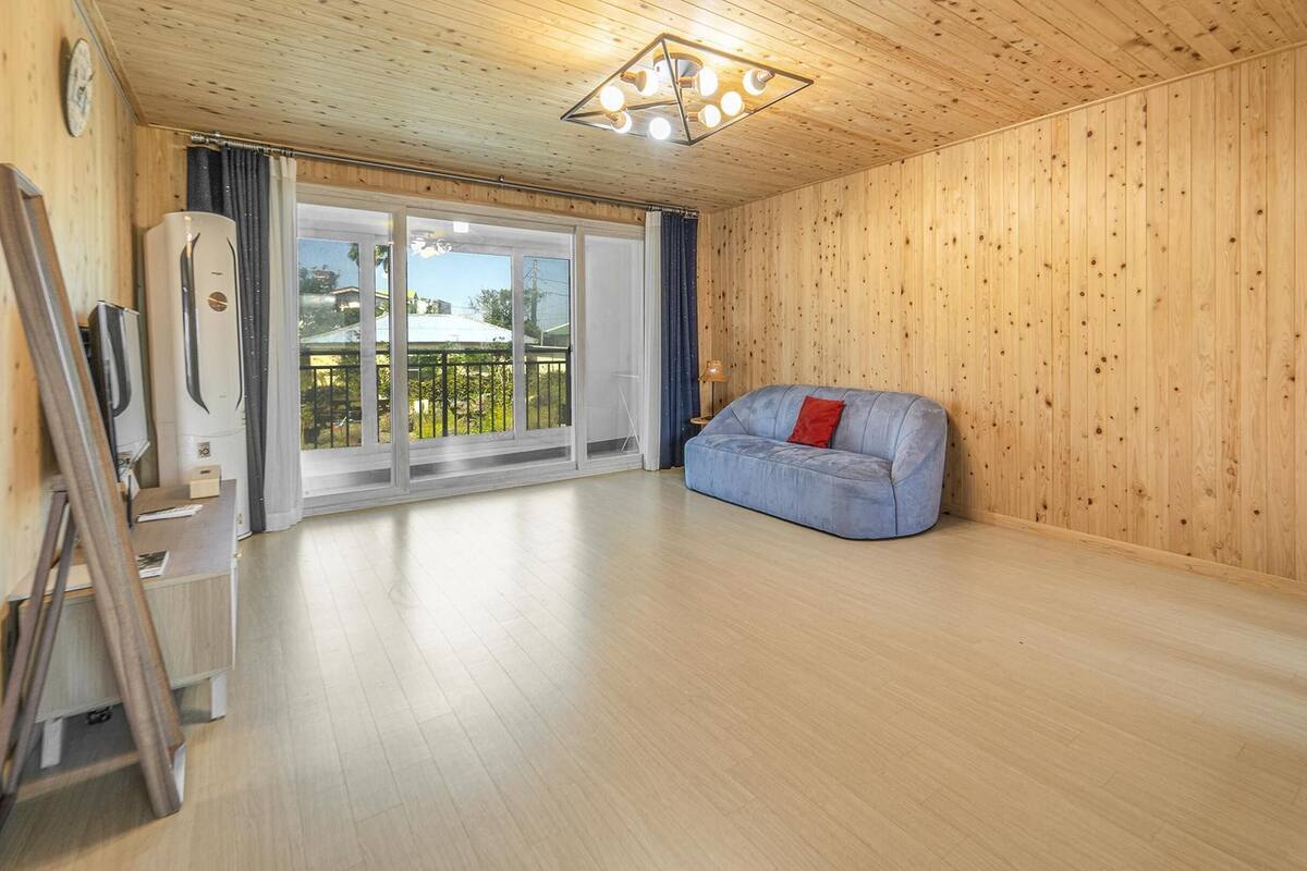 Une pièce spacieuse aux murs en bois et dotée d’une grande porte-fenêtre coulissante donnant sur un balcon.