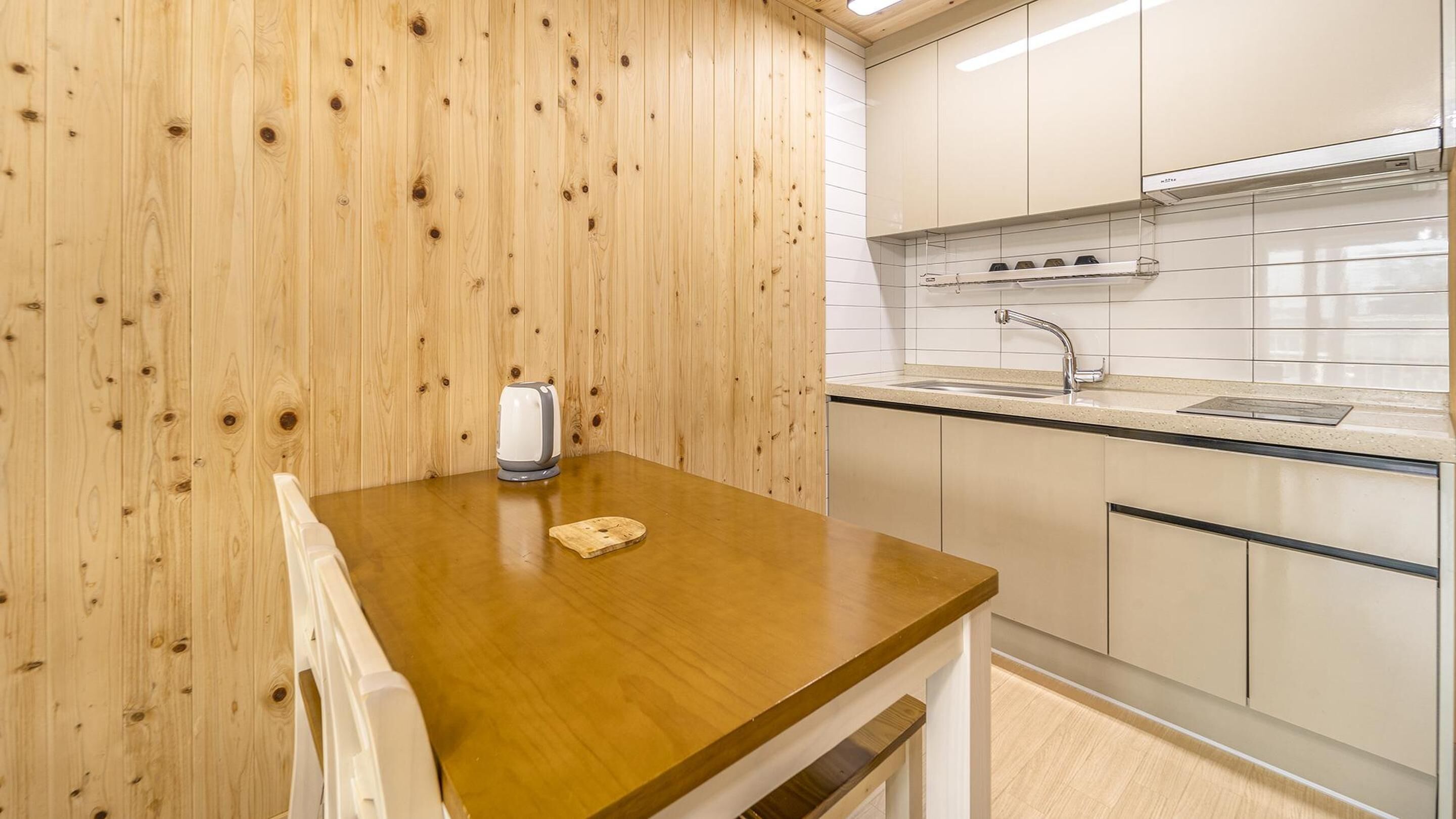A compact kitchen with wooden walls, a wooden countertop, a sink, and white cabinets.
