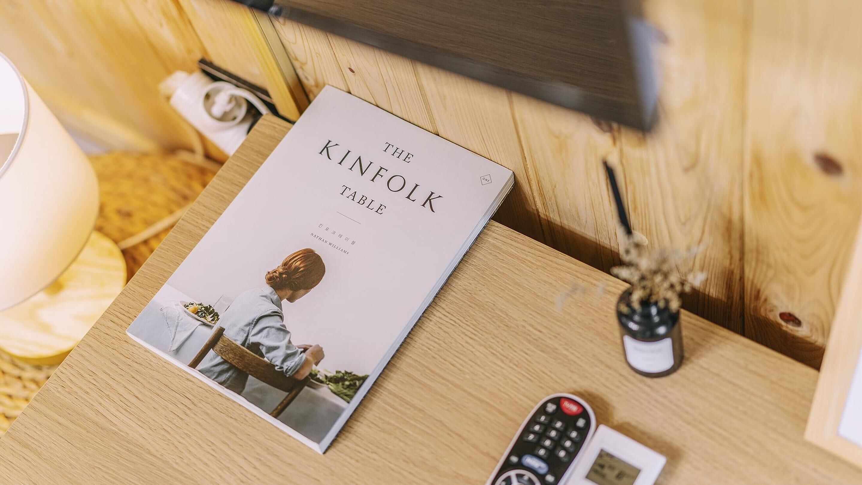 Un livre intitulé « The Kinfolk Table » est posé sur une table en bois, à côté d’une télécommande et d’un petit vase.