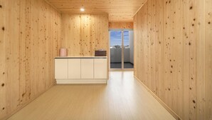 Een hal met houten wanden en een lichtgekleurde vloer, die uitkomt op een balkon met uitzicht op de lucht en gebouwen.