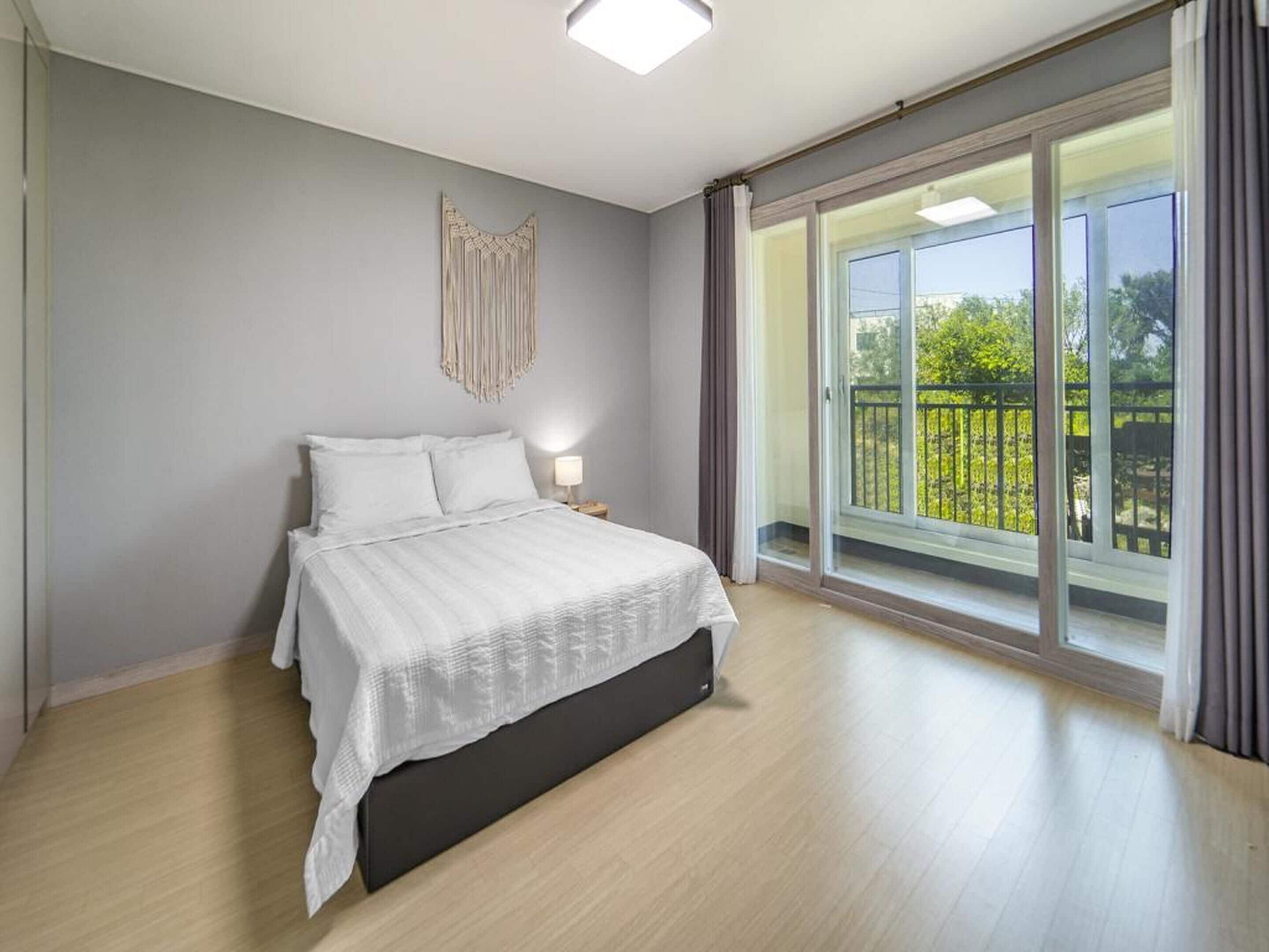A bedroom with a bed, a nightstand, a wall-mounted light, and a large sliding glass door leading to a balcony.