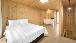 Een slaapkamer met een houten vloer en wanden, een bed met wit beddengoed, een klein nachtkastje en een kast.