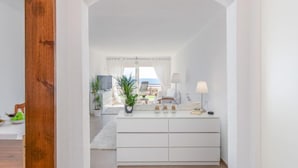 Une pièce moderne et minimaliste, avec une console blanche, un grand miroir et une vue sur un balcon aménagé avec du mobilier d’extérieur.