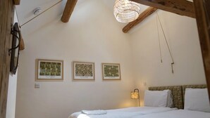 Un dormitorio con cama, toallas blancas, una lámpara colgante y tres cuadros en la pared.