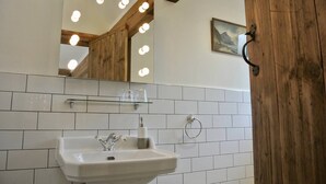 A bathroom with a white sink, a mirror with lights, a wooden wall, and a small shelf with glasses. - Nest Holiday Hideaway Wren Cottage Stunning Area! (Church Stretton)
