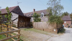 A rustic wooden building with a stone roof, a wooden fence, and a gravel path leading to a house with a brick exterior. - Nest Holiday Hideaway Wren Cottage Stunning Area! (Church Stretton)