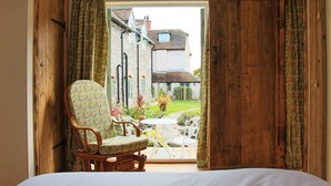 A bedroom with a large bed, wooden door, and a chair facing a garden with a view of a house. - Nest Holiday Hideaway Wren Cottage Stunning Area! (Church Stretton)