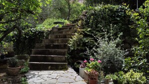 Ein steiniger Weg führt zu einer Treppe, umgeben von üppigem Grün und Pflanzkübeln.