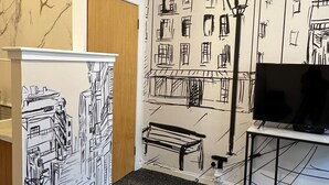 A room with a large wall mural of a cityscape, a clock, a television on a stand, and a bench.