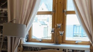 A wooden bed with white bedding, a window with curtains, and a lamp on a shelf.