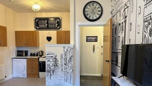 A compact kitchen with wooden cabinets, a microwave, a refrigerator, and a clock on the wall.