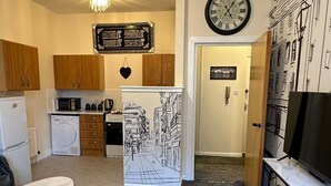 A compact living space with a kitchenette, a dining area, a living room with a TV, and a large wall clock.