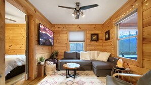 L’intérieur chaleureux d’un chalet, avec un revêtement mural en bois, un canapé, un fauteuil, une petite table et un ventilateur de plafond.