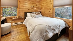 Une chambre dans une cabane en bois, avec un lit, une table de chevet, une chaise et une fenêtre donnant sur la forêt.