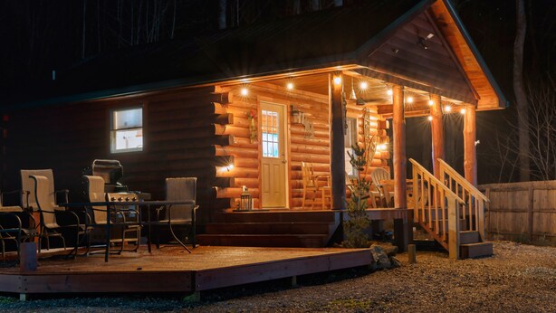 Une cabane en rondins avec un porche, un espace salon extérieur et un barbecue.