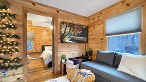L'intérieur d'un chalet confortable, avec un plancher en bois, un canapé gris, une petite table ronde et un tableau représentant un arbre accroché au mur.