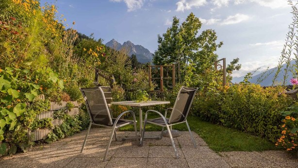 Une terrasse extérieure avec une table et des chaises, entourée d’une végétation luxuriante et offrant une vue sur les montagnes.