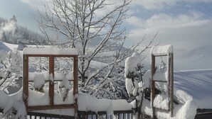 Une porte en bois recouverte de neige, dotée d’un cadre en métal, entourée d’arbres chargés de neige et avec une chaîne de montagnes en arrière-plan.