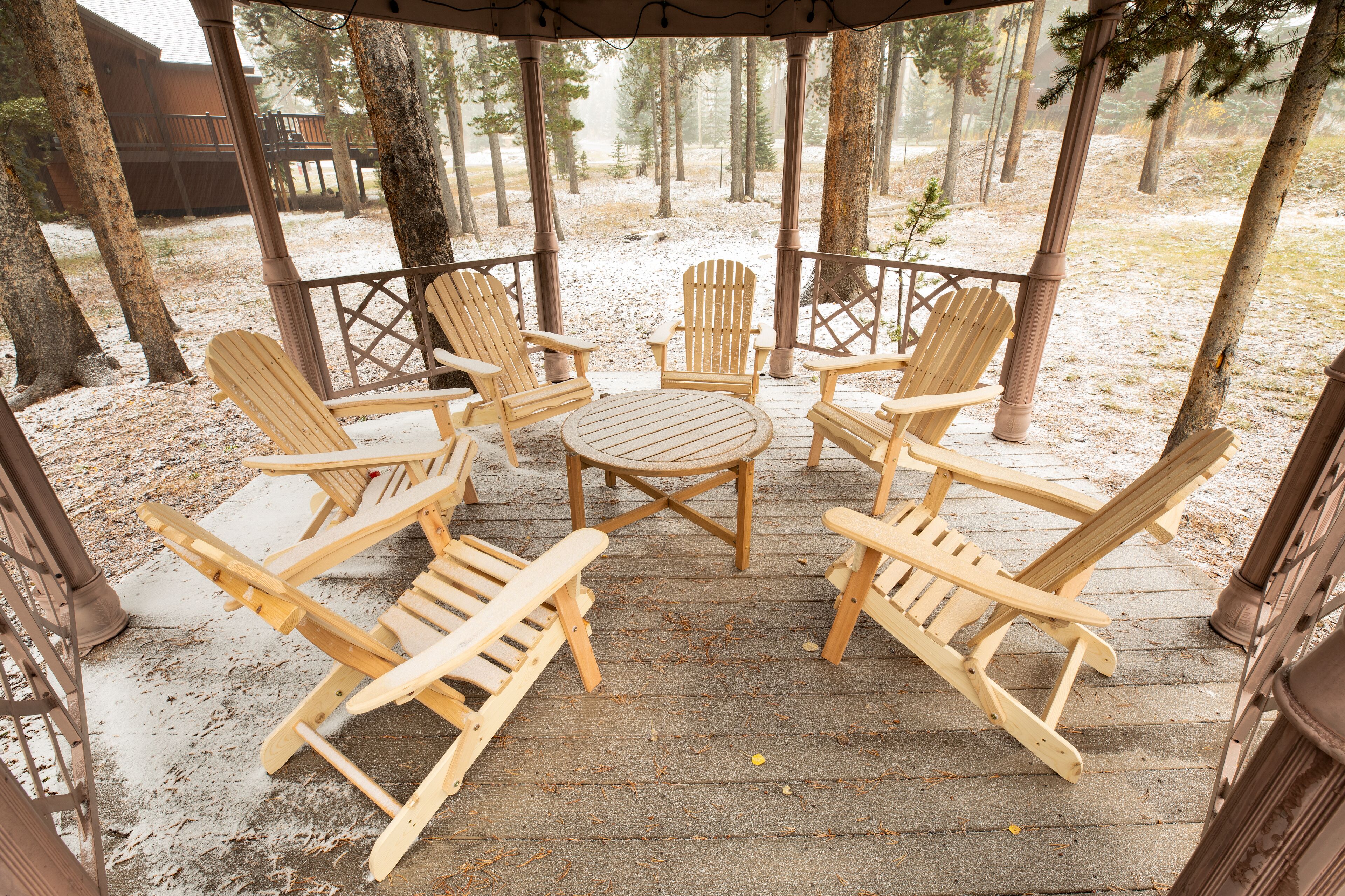 A wooden deck with Adirondack chairs and a table, surrounded by trees.
